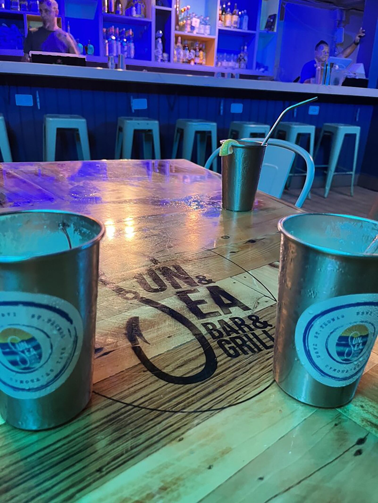 Zona de bar amb taula de fusta, gots metàl·lics i barra.