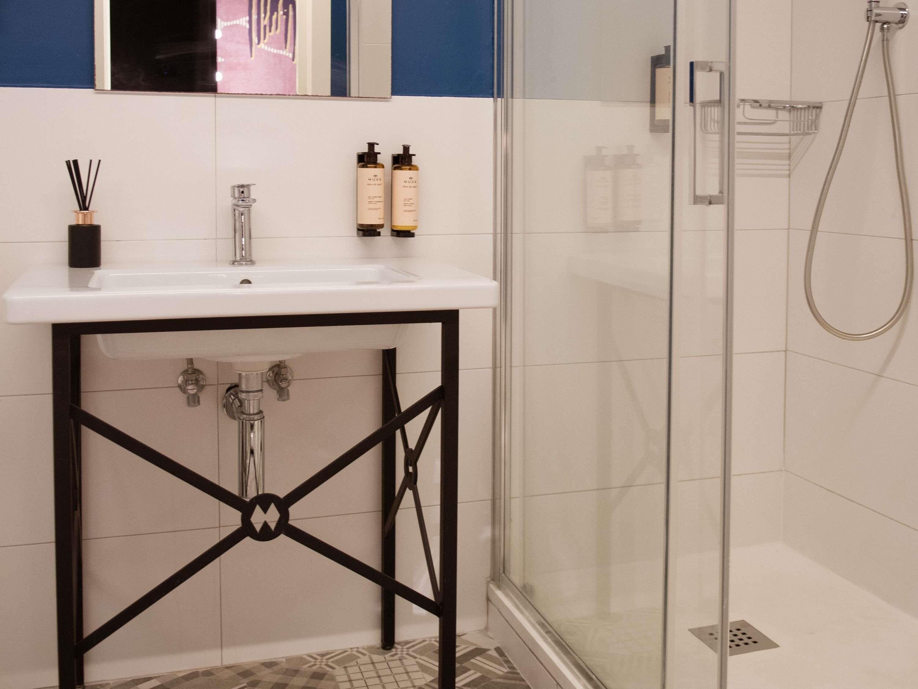 Un baño con lavamanos blanco, estructura metálica negra y cabina de ducha de vidrio.