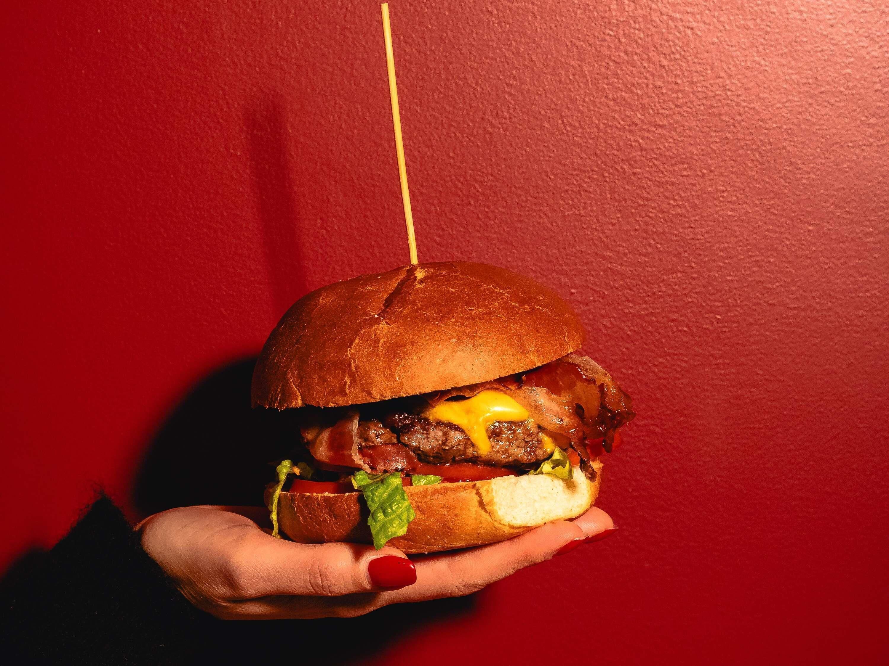 Una mano sosteniendo una hamburguesa con un palillo.