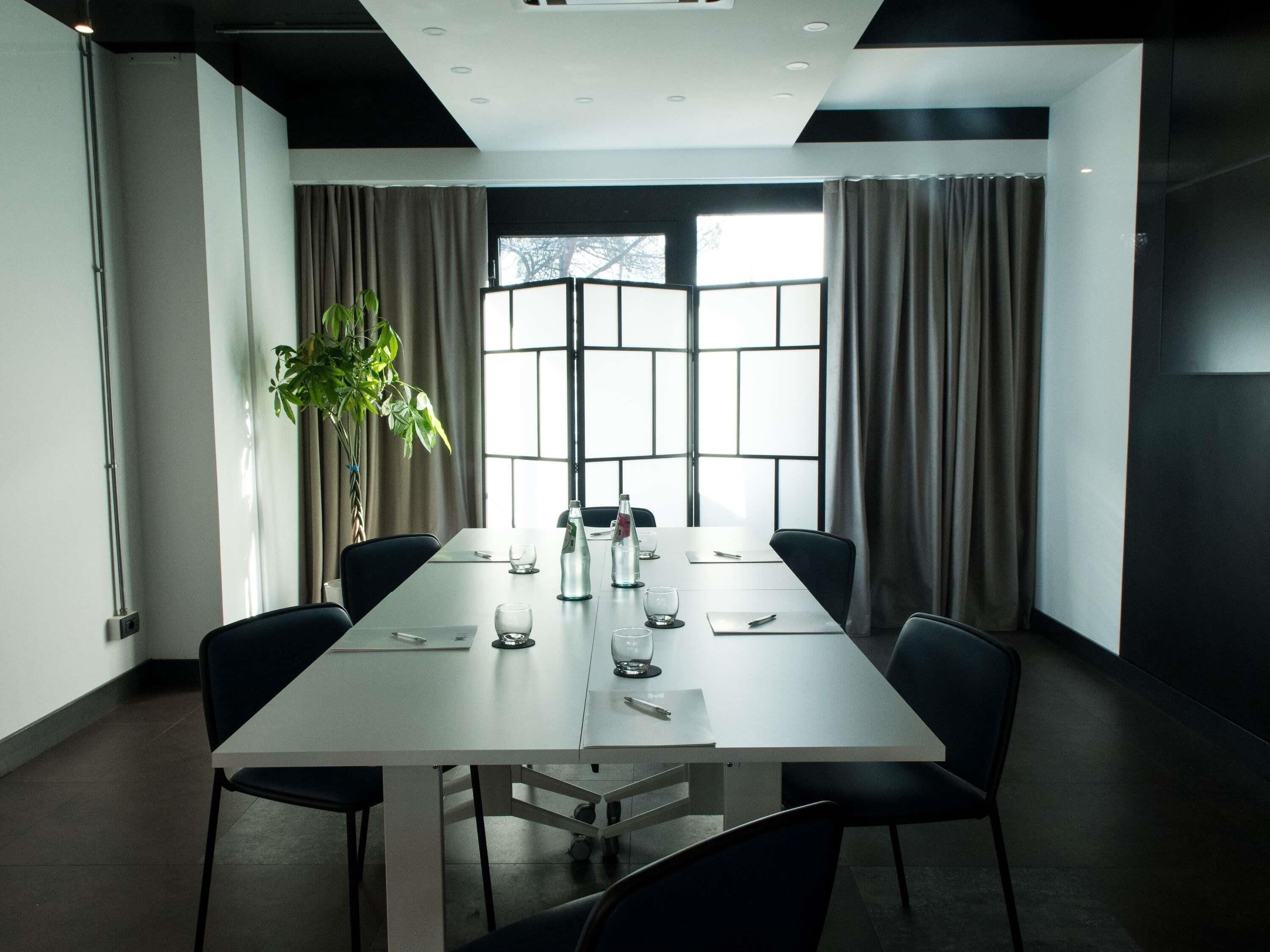 A conference room with a long table, chairs, a potted plant, and large windows with curtains.