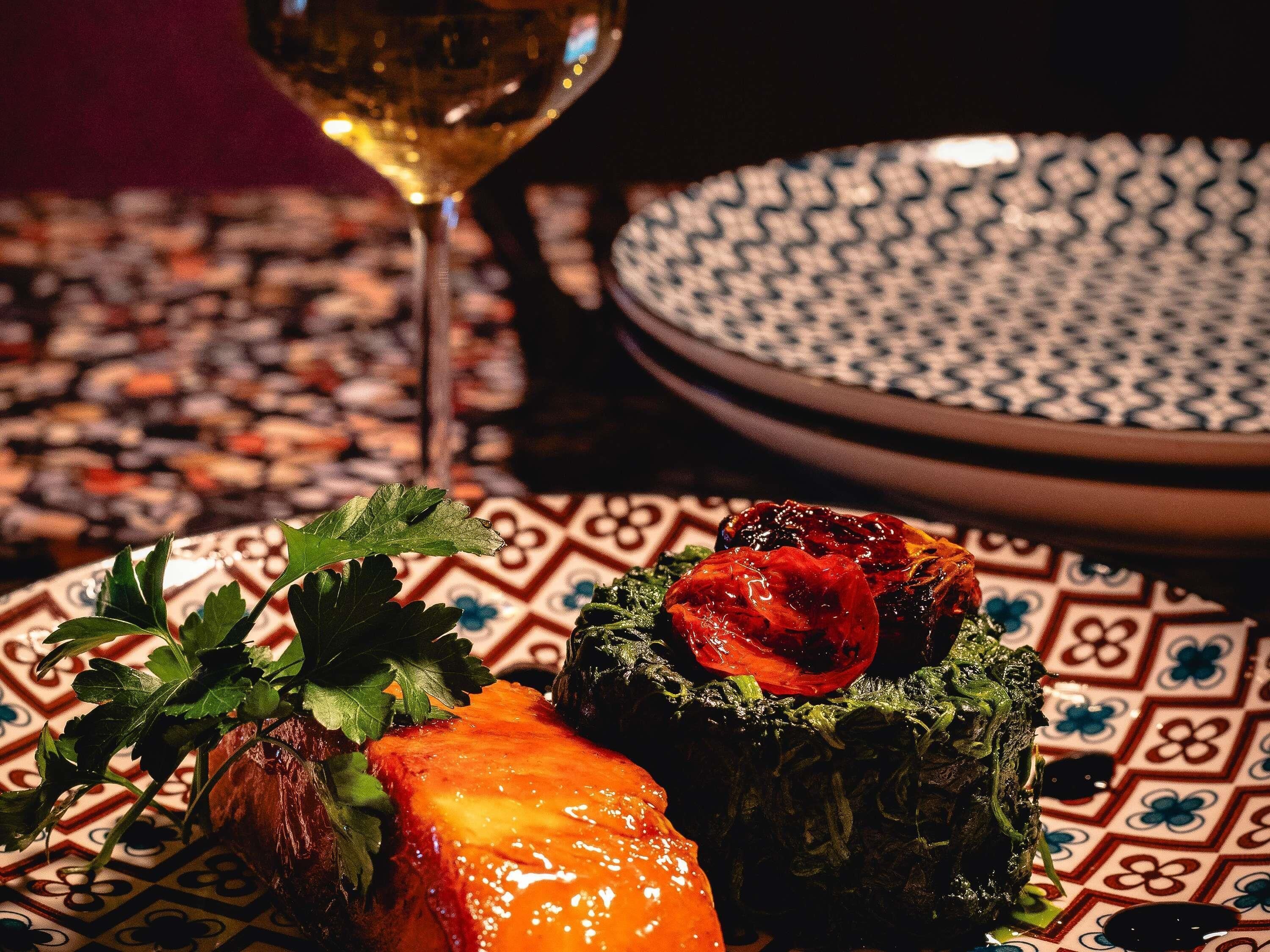 A plate with a stuffed pepper, a glass of white wine, and a patterned tablecloth.