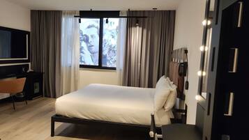 A modern hotel room with a bed, a desk, a chair, a television, and a window with curtains.