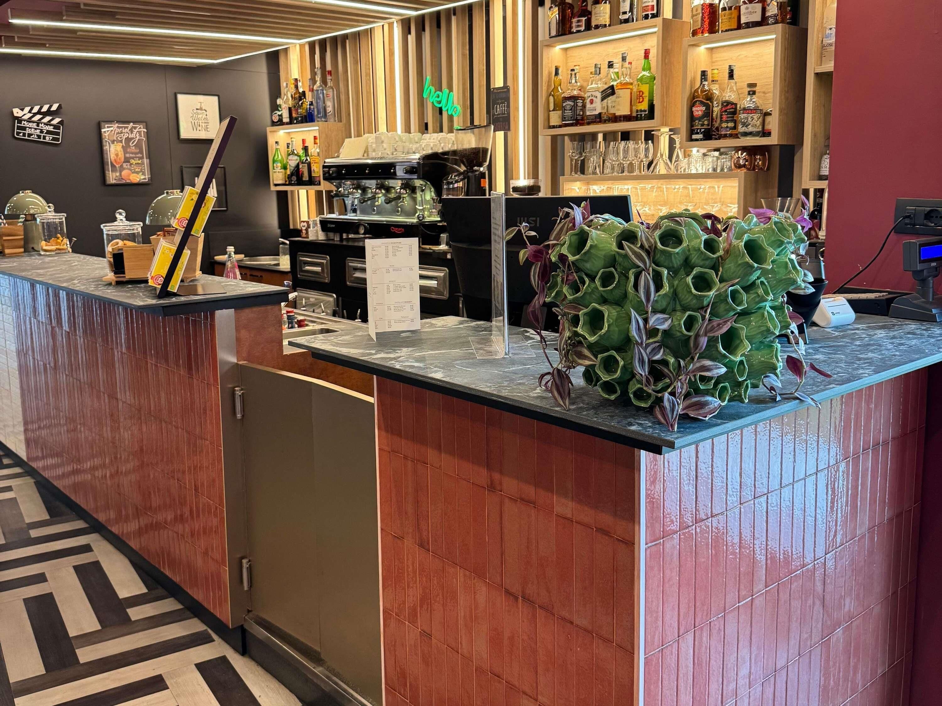 Una zona de bar con mostrador, taburetes, una máquina de café y un letrero de neón que dice 'hello'.