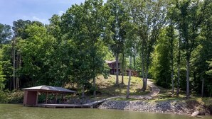 A lakeside cabin with a dock and a covered area, surrounded by dense forest. - Come have fun in the sun on the Tennessee River with a private dock (Loudon)
