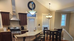 A modern kitchen with a central island, bar stools, a dining area with a table and chairs, and a cozy seating area with a couch. - Come have fun in the sun on the Tennessee River with a private dock (Loudon)