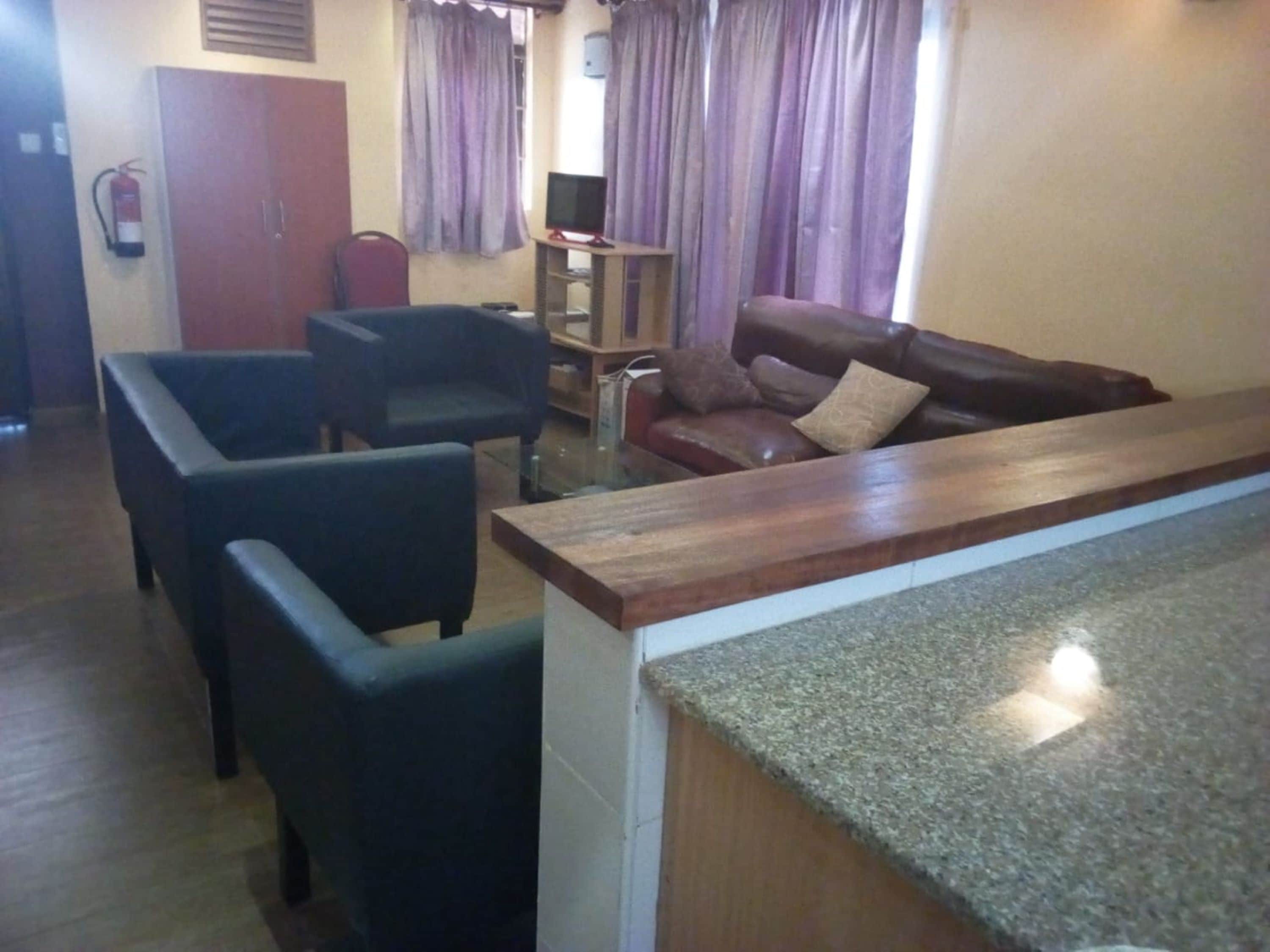 A living room with a brown leather sofa, two black armchairs, a small wooden coffee table, and a TV on a stand.