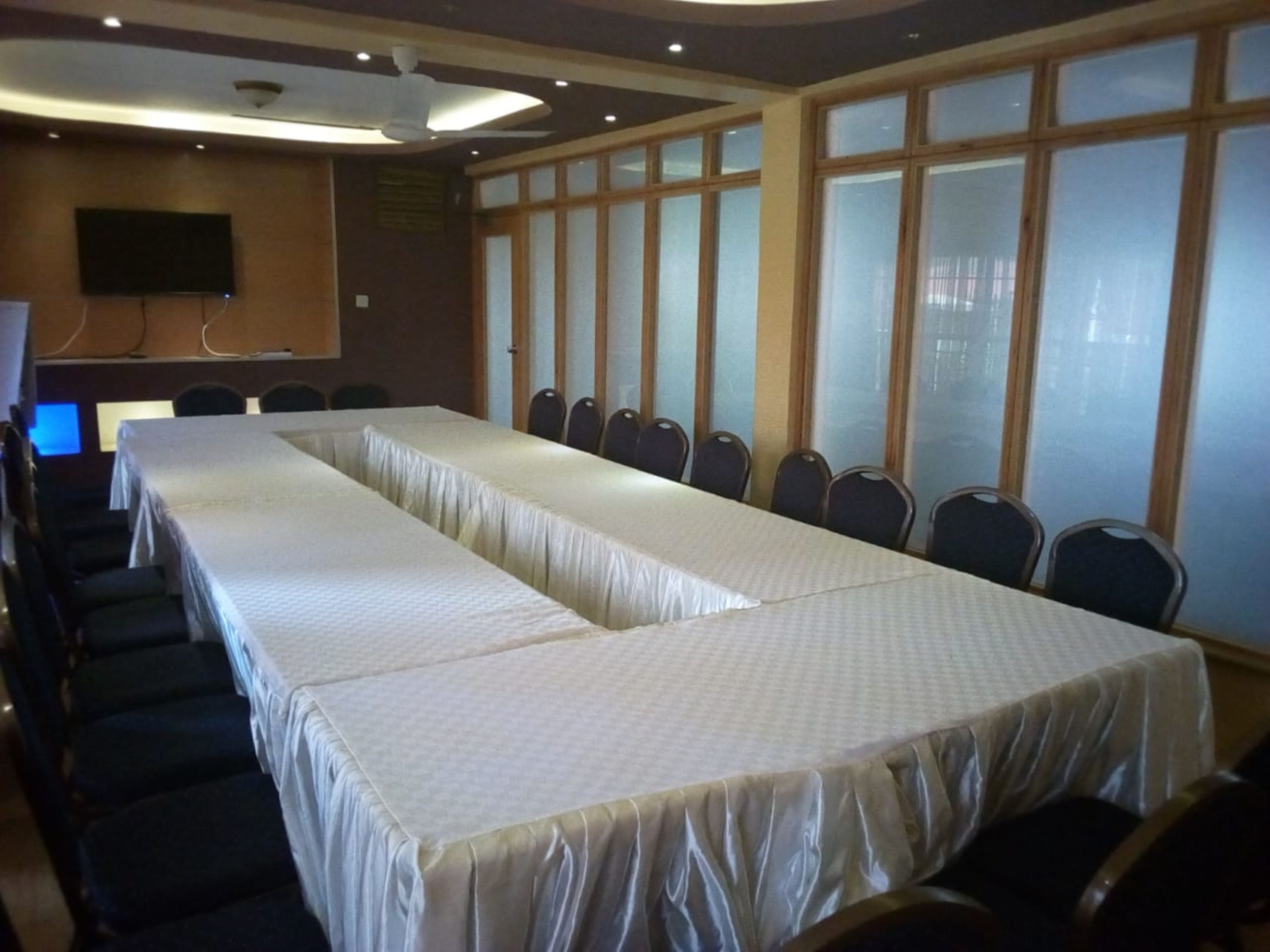 Un salón de conferencias con mesas largas, sillas, un televisor de pantalla plana y ventanas amplias.