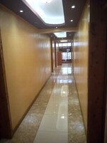 Corredor com paredes de madeira e piso ladrilhado brilhante, que conduz a uma área luminosa com janelas.
