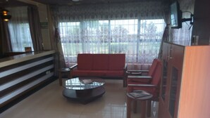 A spacious living room with a red sofa, a glass coffee table, and wooden chairs. A staircase is visible in the background, leading to an upper floor.