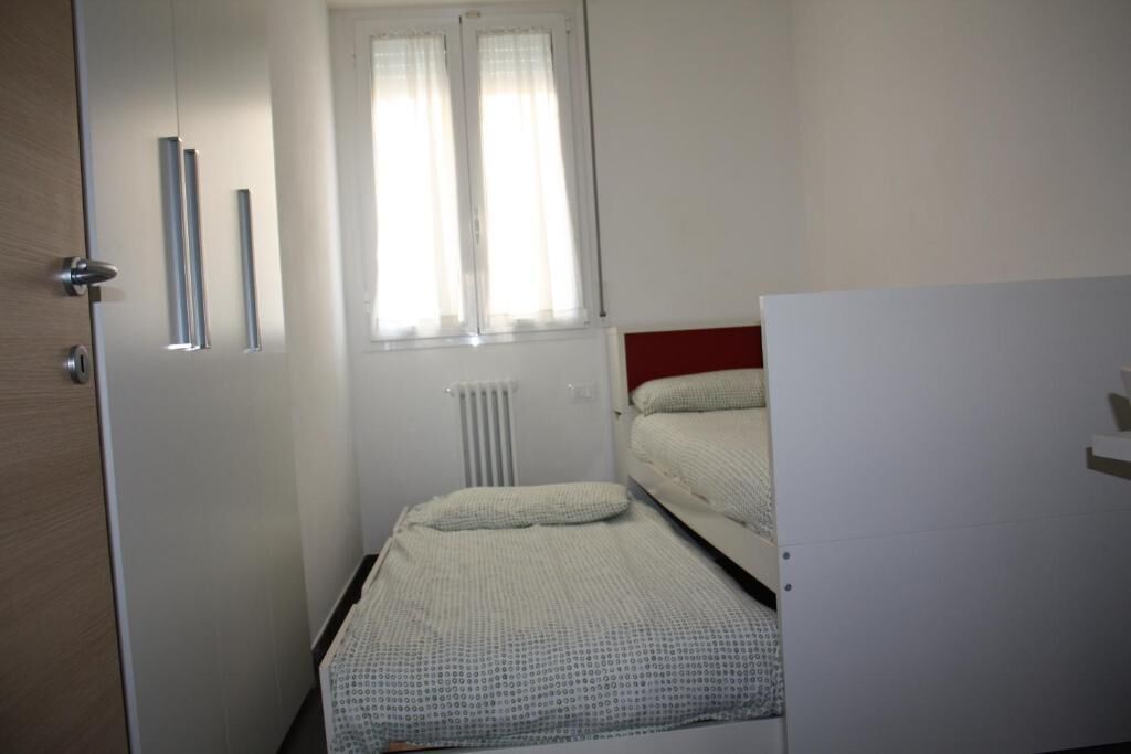 Una habitación pequeña y funcional con dos camas individuales, un radiador y una ventana con cortinas.