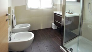 Un baño moderno con inodoro, bidé y ducha con mampara de vidrio.