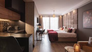 Ein modernes Hotelzimmer mit Küchenzeile, einem Bett mit vielen Kissen, einem Essbereich und einem kleinen Tisch mit einer dekorativen Lampe.