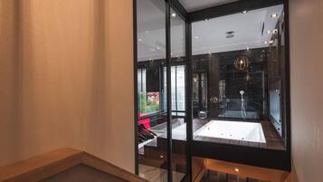 A modern interior with a glass wall, a wooden staircase, and a visible bathroom with a bathtub.