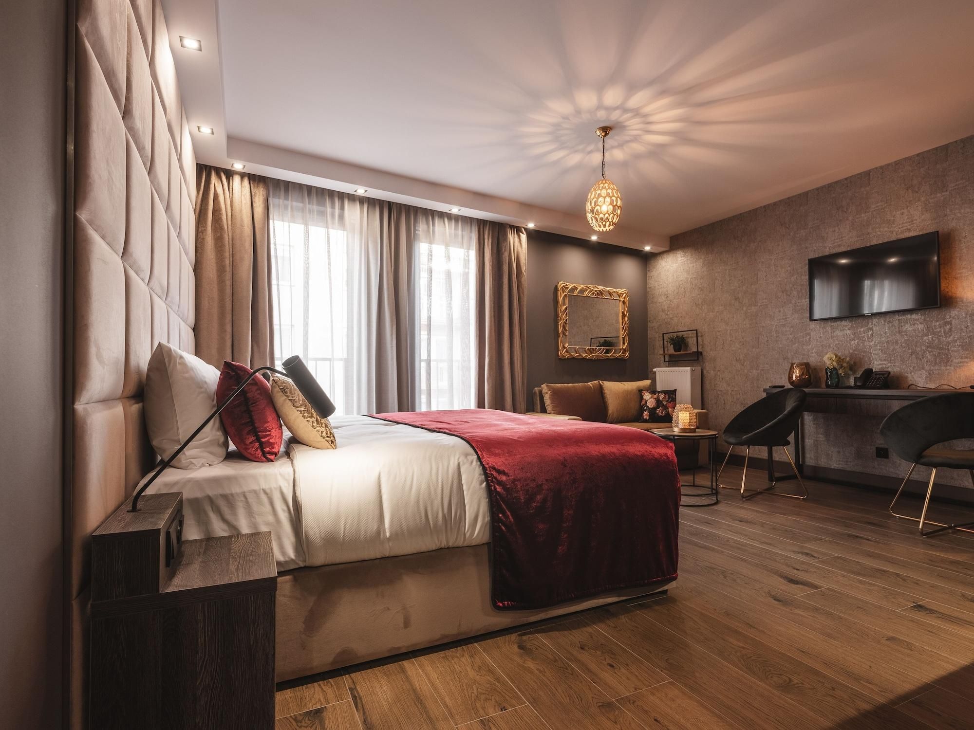 A modern hotel room with a large bed, a desk, a TV, and a chandelier.