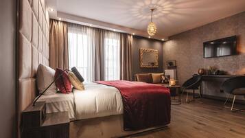 A modern hotel room with a large bed, a desk, a TV, and a chandelier.