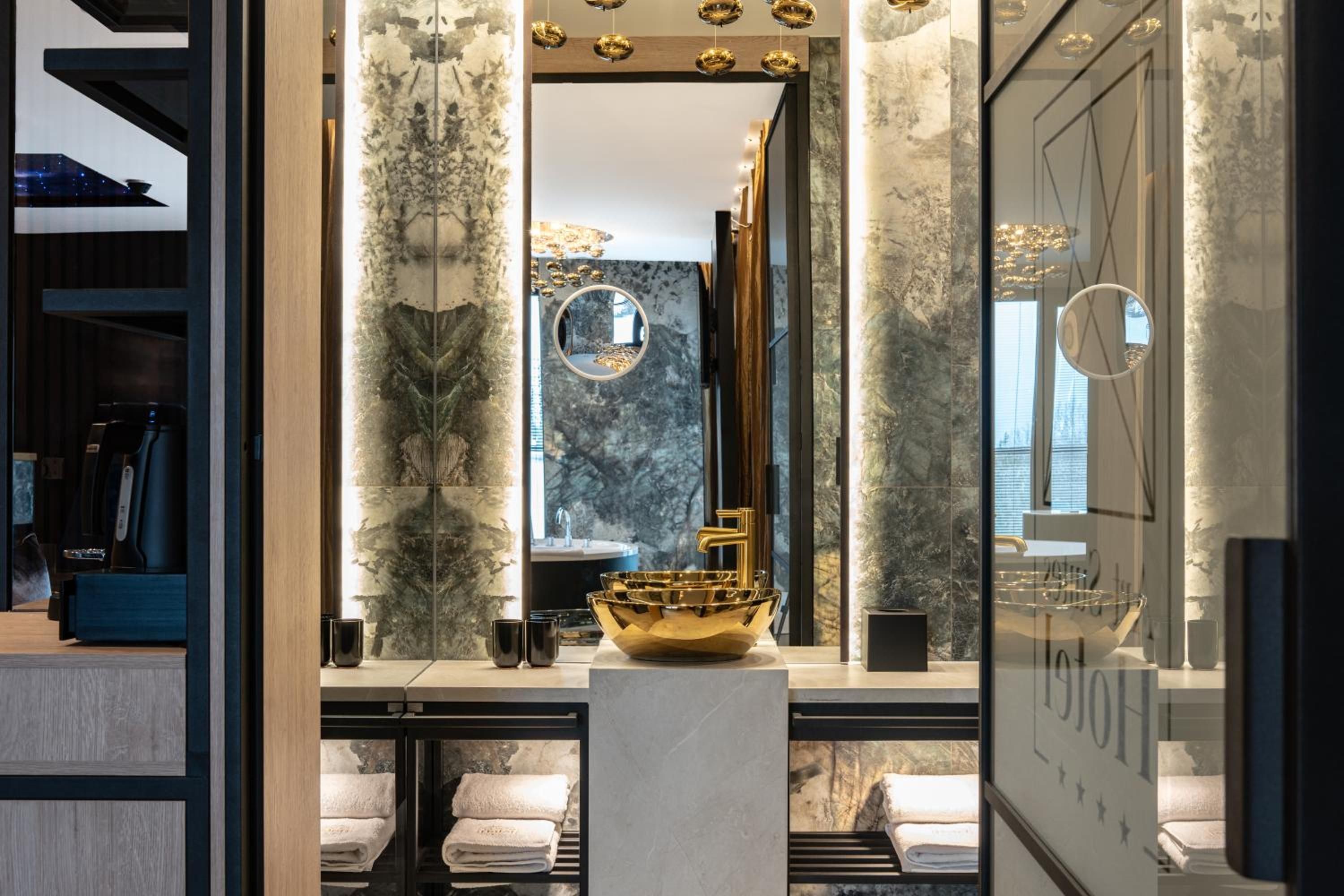 Ein modernes Badezimmer mit Marmorwand, einem goldenen Waschbecken und einem großen Spiegel.