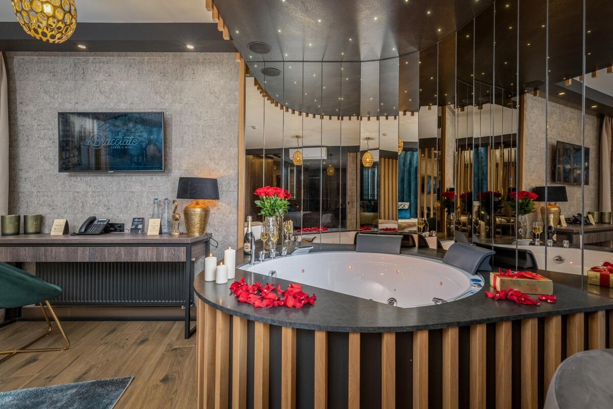 A modern hotel lobby with a reception desk, a large mirror, and a central seating area with a round table.