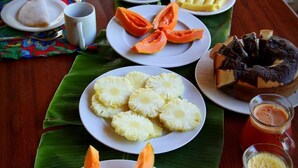 A table with various dishes including sliced pineapple, cantaloupe, and a cake, along with beverages. - Pousada Albergue da Jangada (São Miguel do Gostoso)