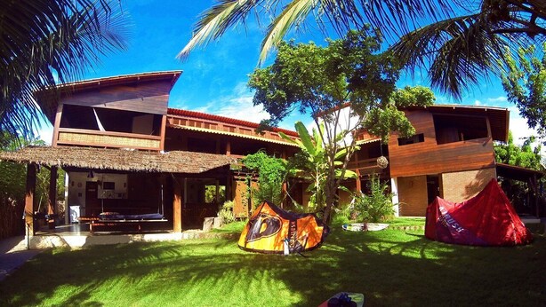 A tropical resort with a wooden deck, a thatched-roof structure, and a red tent. - Pousada Albergue da Jangada (São Miguel do Gostoso)