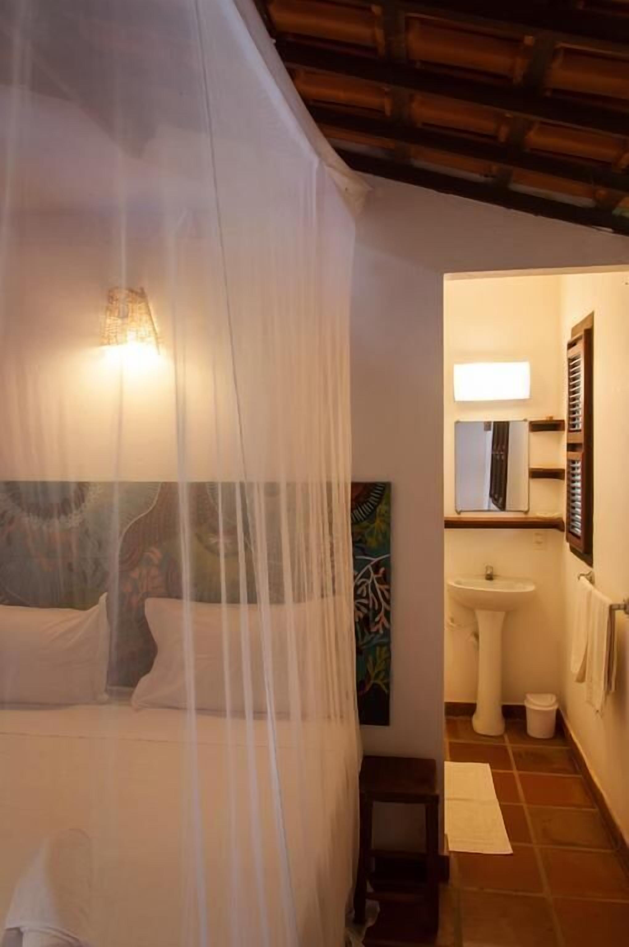 A bedroom with a canopy bed, a bedside lamp, a small table, and a painting on the wall.
