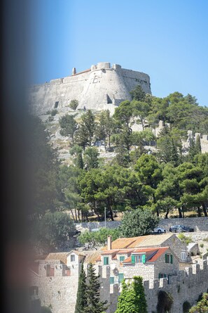 A historic stone castle on a hill with surrounding trees and traditional buildings. - Apartments Stipisic (Hvar)