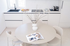 Una cocina moderna con armarios blancos, una mesa redonda para comer y un florero con ramas.