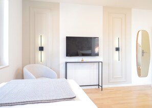 A modern hotel room with a bed, a television on a stand, a chair, and a large mirror.