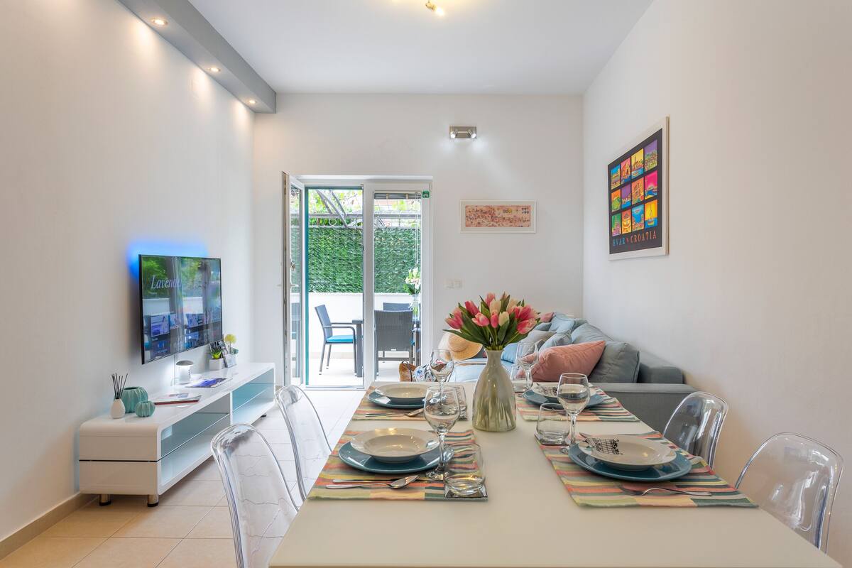 A modern dining area with a table set for four, clear chairs, a glass-top console table, and a television on the left.
