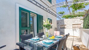 An outdoor dining area with a glass table, wicker chairs, and a brick wall. - Apartments Stipisic (Hvar)