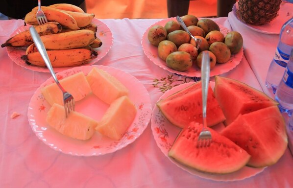 Una mesa con platos de frutas, incluyendo plátanos, mangos y rebanadas de sandía.