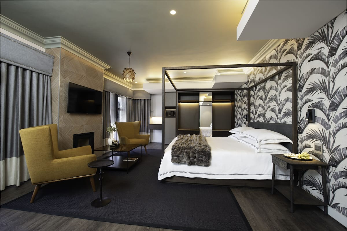 Una habitación de hotel moderna con una cama grande, una zona de estar con una silla y una mesa, un televisor de pantalla plana y una pared decorativa con un motivo de hojas.