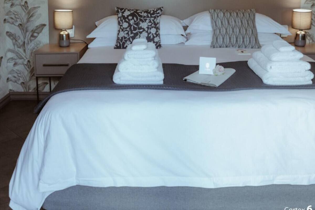 Una habitación de hotel con una cama grande, dos mesitas de noche con lámparas, un cabecero y un estampado floral en el papel tapiz.