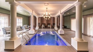 Une grande piscine intérieure au design moderne, entourée de colonnes et agrémentée d’un espace détente avec des fauteuils.