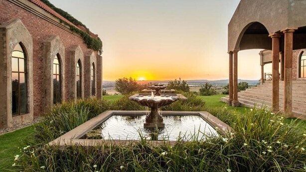 Une cour intérieure avec une fontaine centrale, des arcades en briques et une vue sur le coucher du soleil.