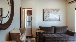 Un salon avec un canapé gris foncé, une table basse en bois et un grand tableau abstrait accroché au mur.