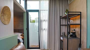 Un intérieur moderne avec un canapé en cuir, un plancher en bois, un coin cuisine où se trouve un chien, et une vue à travers une porte vitrée.
