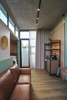 Un interior moderno con un sofá de cuero, piso de madera, una zona de cocina con un perro y vistas a través de un ventanal.