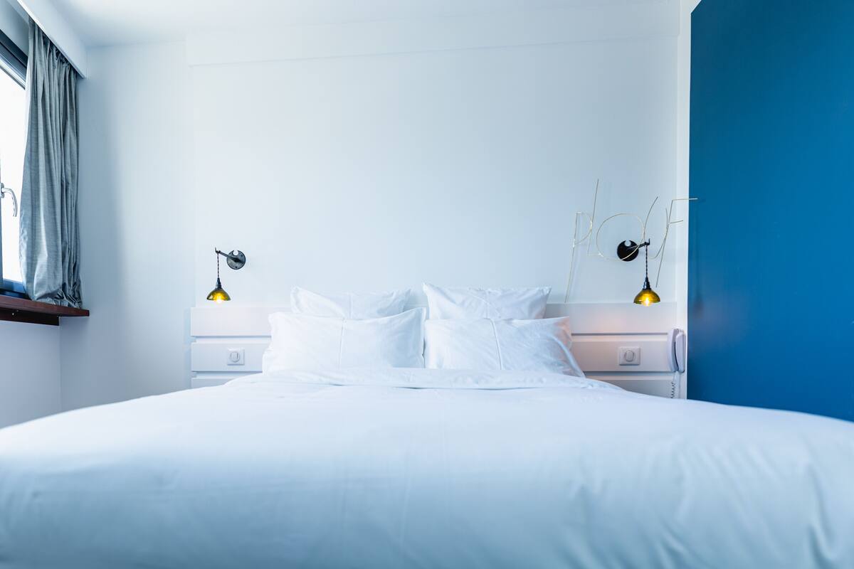 Un dormitorio moderno con una cama grande, ropa de cama blanca, dos lámparas de noche y una pared azul.