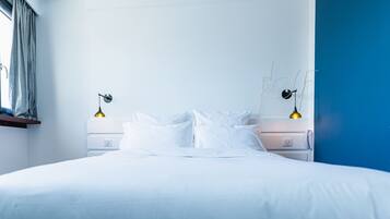 A modern bedroom with a large bed, white bedding, two bedside lamps, and a blue accent wall.