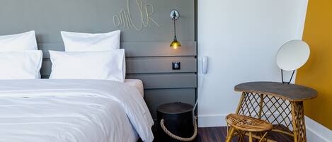 A bedroom with a bed, bedside table, lamp, and a small round table with a chair.
