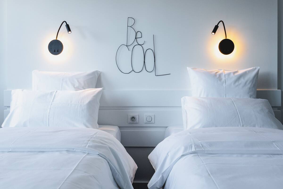 Un dormitorio con dos camas, una lámpara fijada a la pared y una frase motivadora.