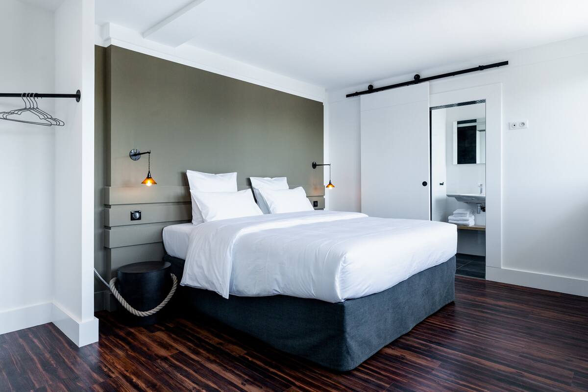 Un dormitorio moderno con una cama grande, lámparas de noche, una mesita redonda y un perchero.