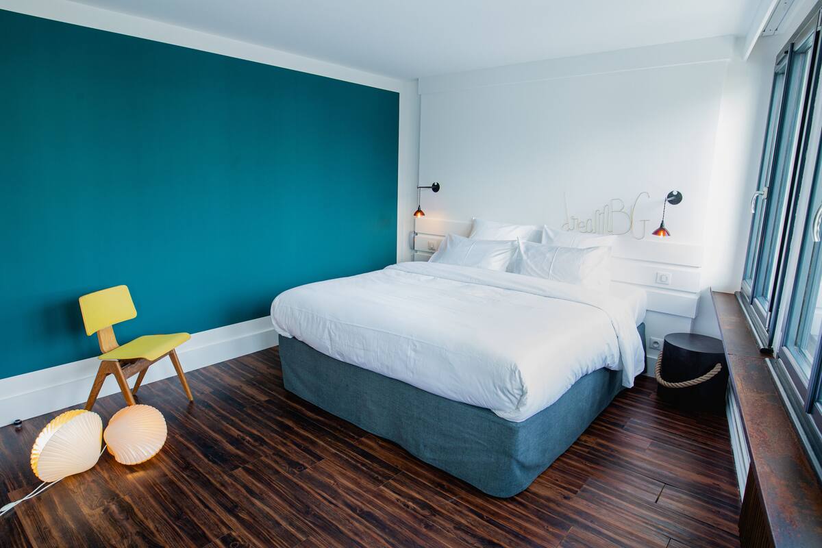 Un dormitorio con una cama, una silla, lámparas de noche y una ventana.