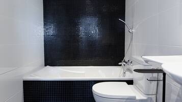 Un baño moderno con una bañera blanca, un inodoro blanco y una zona de ducha con azulejos negros.