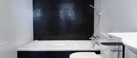 Un baño moderno con una bañera blanca, un inodoro blanco y una zona de ducha con azulejos negros.