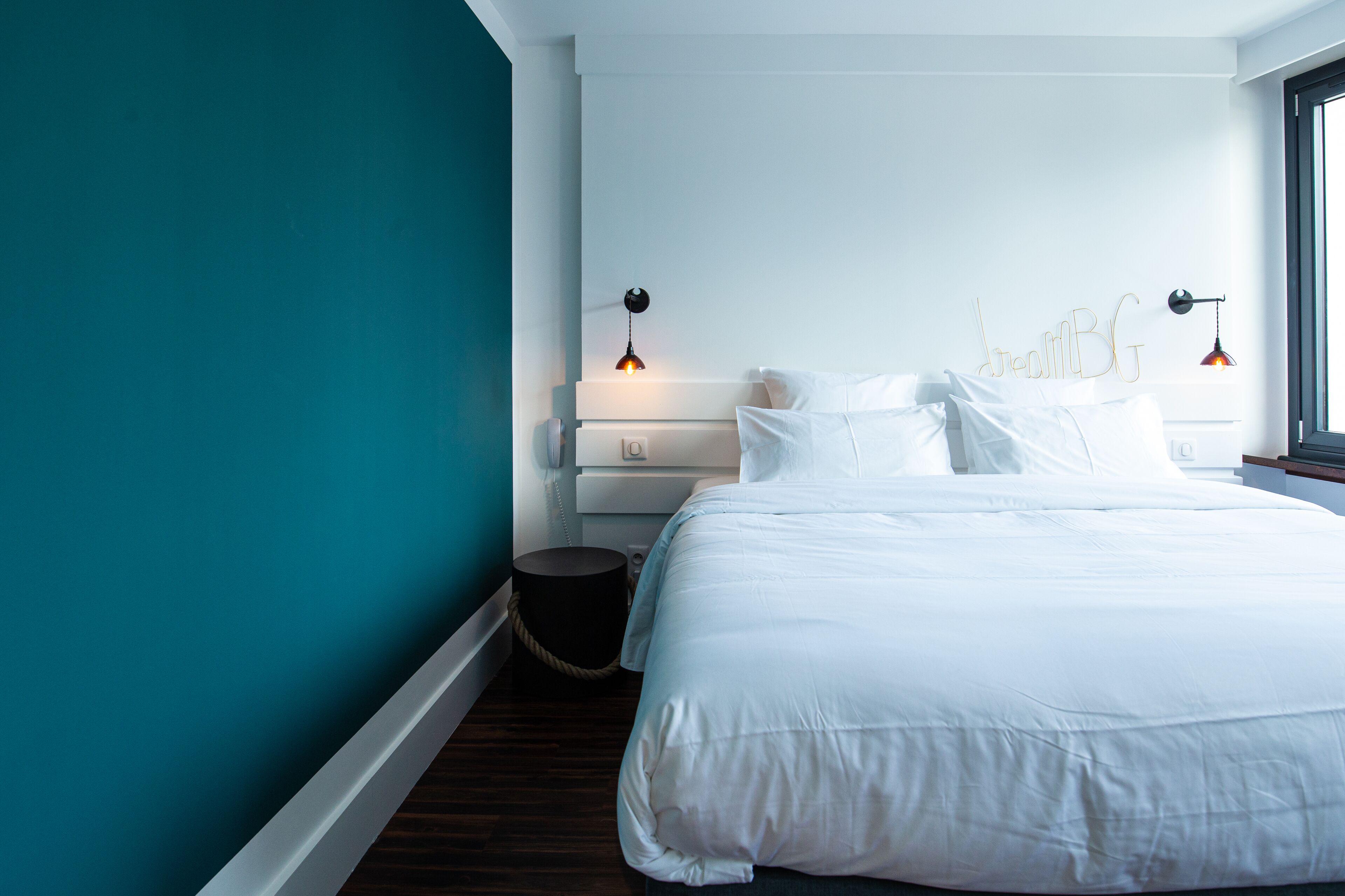Una camera da letto moderna con un letto grande, pareti color petrolio e due lampade a sospensione.