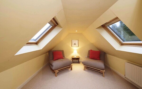 A small attic bedroom with two single beds, a nightstand, a framed picture on the wall, and skylights.