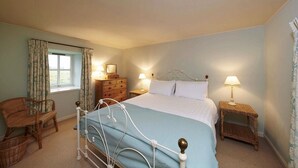 Quarto com cama, duas mesas de cabeceira com luminárias, cômoda, cadeira e janela com cortinas.