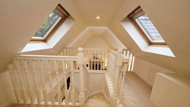 Um quarto de sótão amplo, com teto inclinado, duas claraboias e uma escada de madeira.