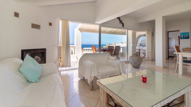 A spacious living room with a white sofa, a glass coffee table, and a view of the sea through large glass doors. - Casa Monsoria - sea views, private pool, walking distance to beach & town centre (Carvoeiro)